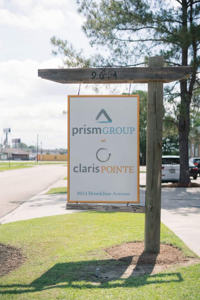Sign for “prismGROUP at clarisPOINTE” offering workers’ compensation mediation stands by a grassy roadside.