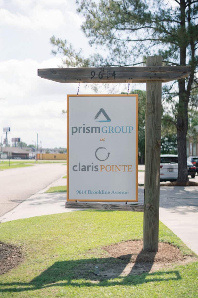 Sign for “prismGROUP at clarisPOINTE” offering workers’ compensation mediation stands by a grassy roadside.