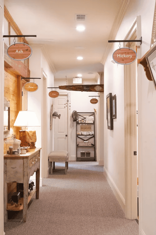 A hallway with labeled room signs, a console table lit by a lamp, shelves, and workers’ compensation mediation info on display.