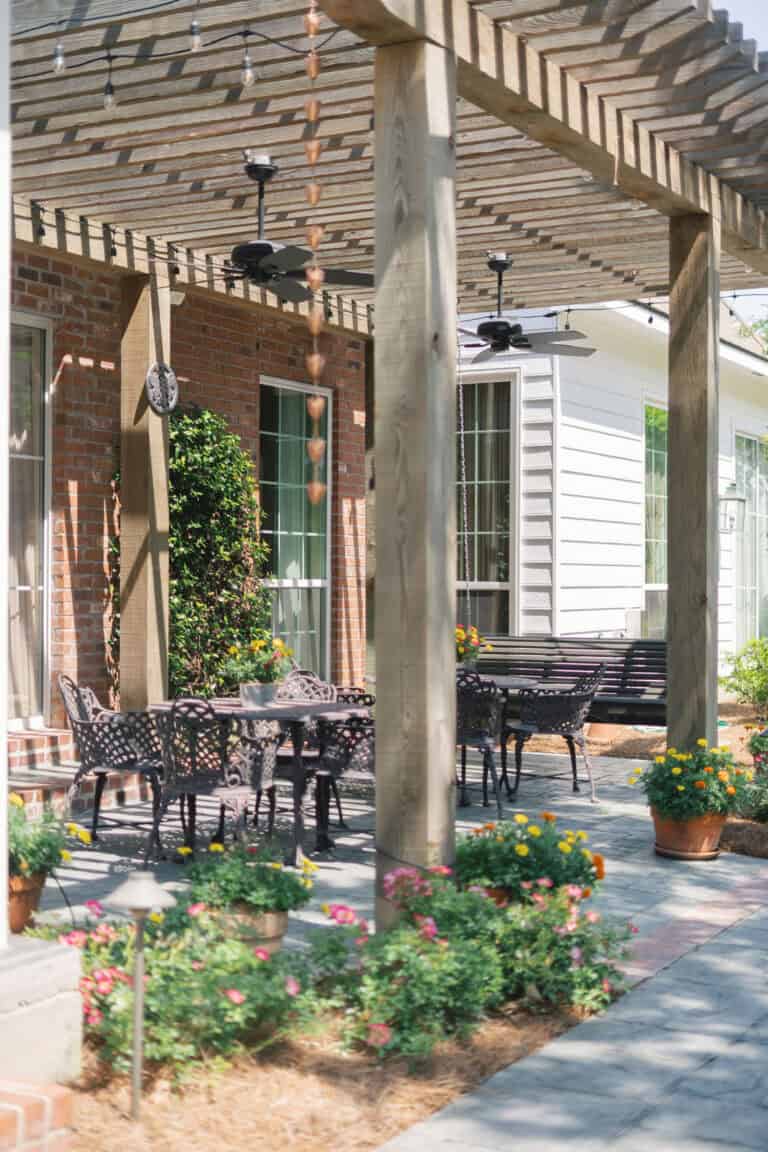 Patio with metal tables and chairs beneath a wooden pergola, surrounded by potted flowers and brick walls—ideal for mediation talks.
