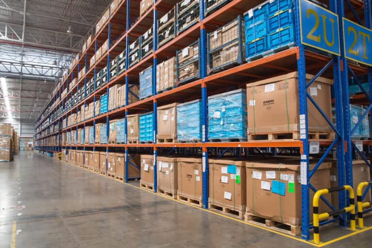 Spacious warehouse with stacked pallets and boxes on labeled shelves, suitable for workers’ compensation logistics needs.