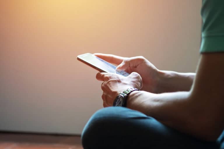 Person sits holding a smartphone, wearing a watch, likely searching for workers’ compensation mediation services.