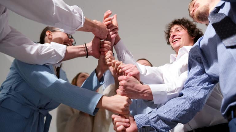Professionals in business attire form a circle, placing their hands together to convey unity in legal mediation.
