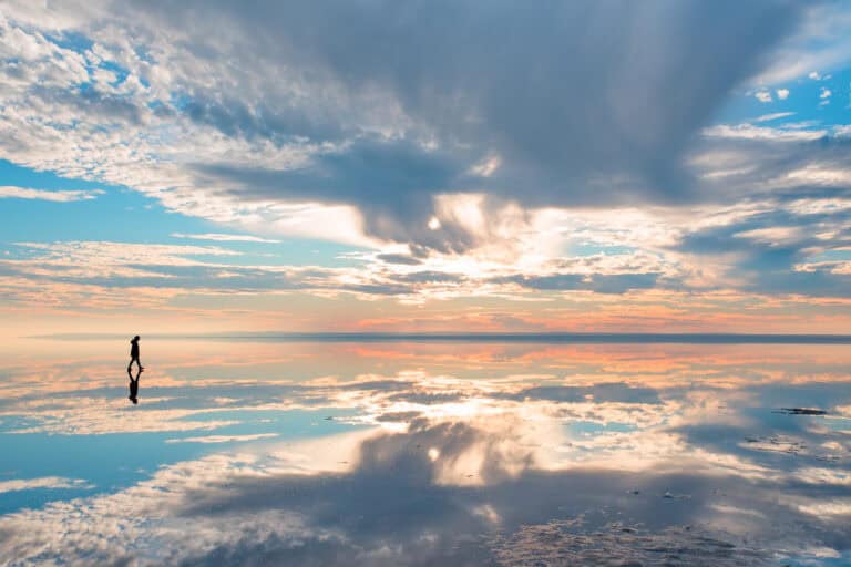A lone figure walks on a reflective surface at sunset, symbolizing the calm and balance of legal mediation services.