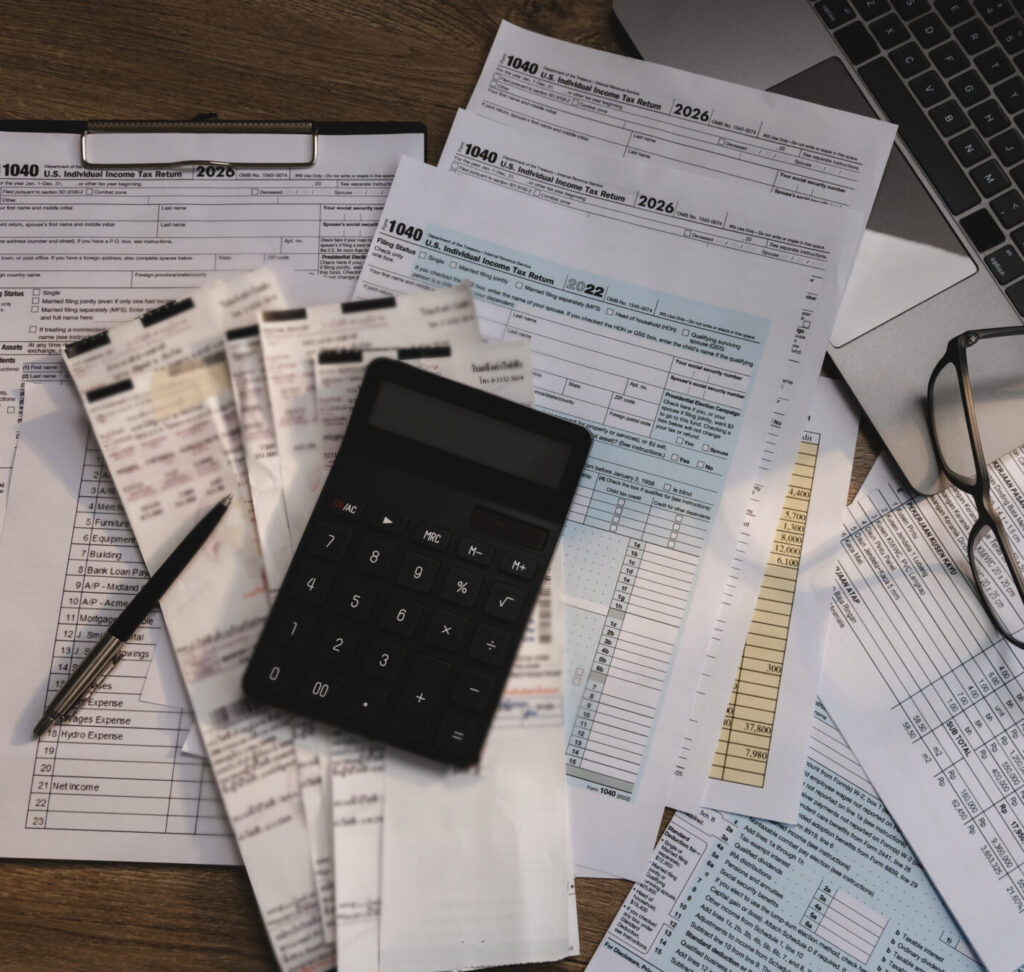 A calculator, pen, and tax forms sit on a desk beside a laptop, common items in compensation legal mediation.