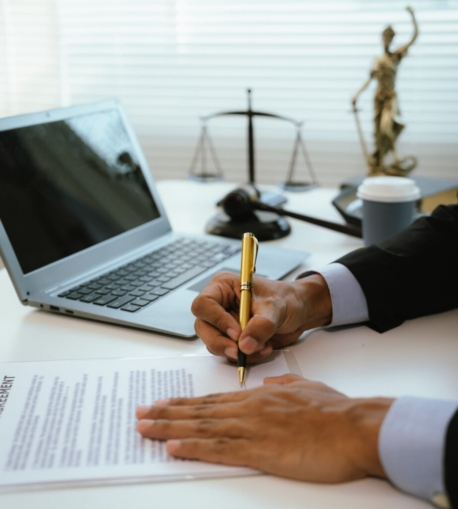 A person in a suit signs paperwork at a desk, with justice symbols behind them, representing legal mediation.