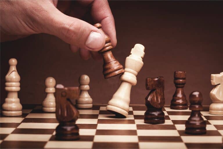 A hand moves a black king toward a white king on a chessboard, symbolizing mediation resolving complex disputes.