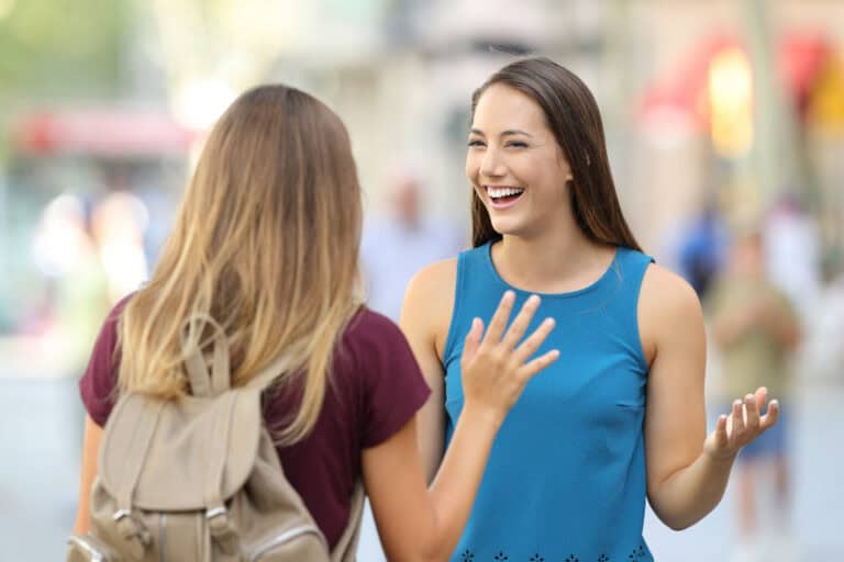 Two young women chat animatedly outdoors, smiling and gesturing as they discuss mediation services face-to-face.