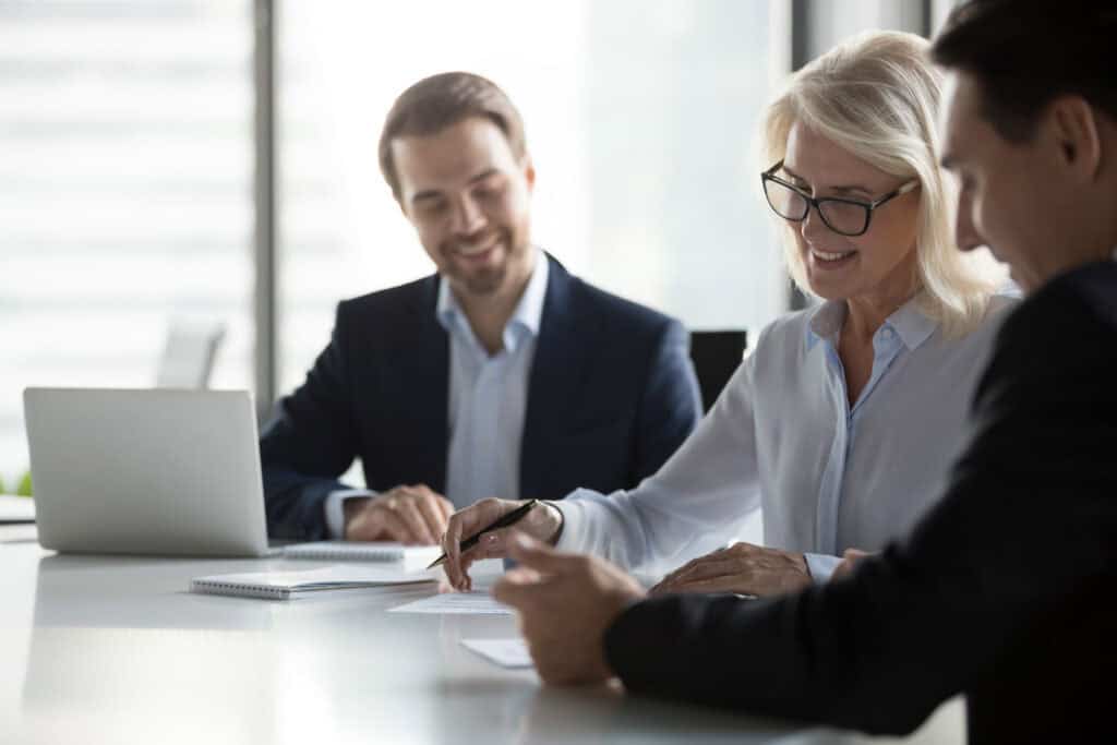 Three professionals sit at a table in a bright office, having a discussion about workers’ compensation mediation.