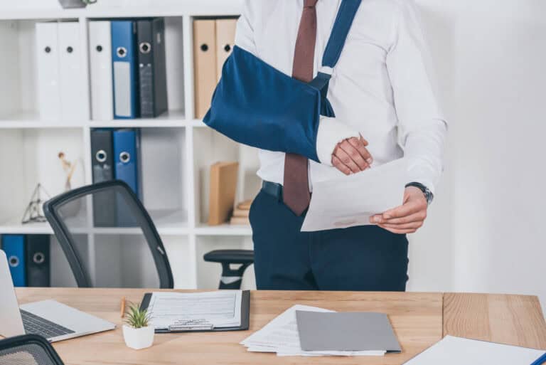 A person in a suit with an arm in a blue sling stands by a desk, representing legal mediation in an office environment.