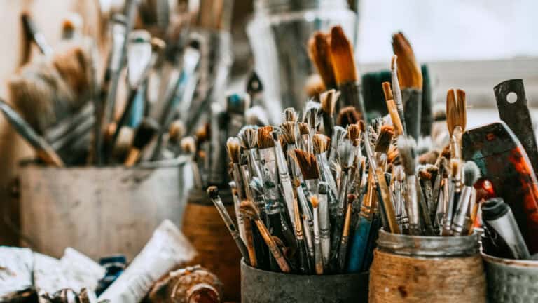 Containers filled with various paintbrushes, tubes, and art supplies suitable for artists or mediation experts.