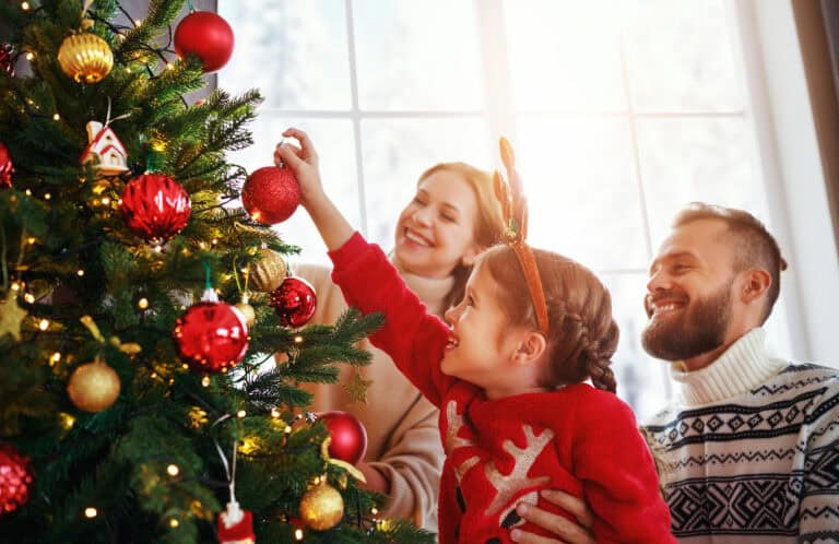 A child hangs a red ornament on a Christmas tree, smiling with two adults—like finding harmony through legal mediation.