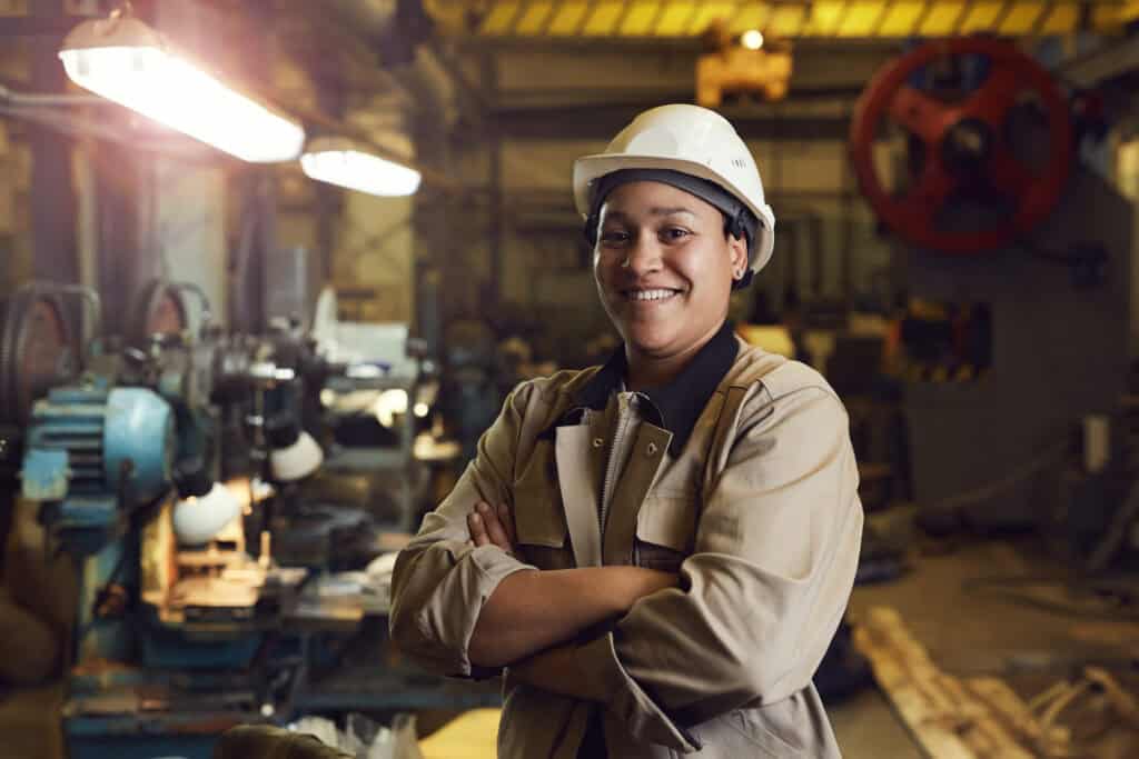 A person in a hard hat stands confidently in an industrial workshop, skilled in workers’ compensation mediation.