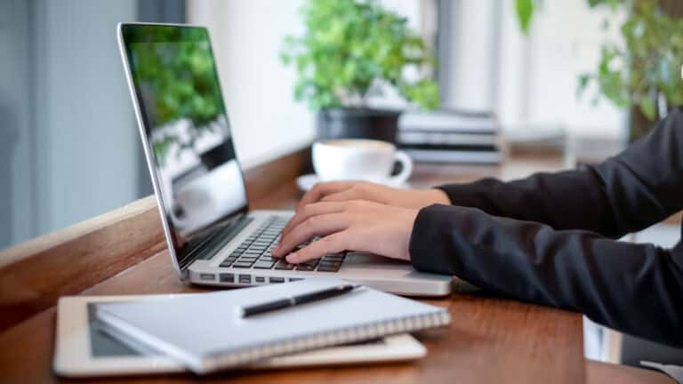 Person working on legal mediation services at a wooden desk with a laptop, coffee, plants, and a notebook.