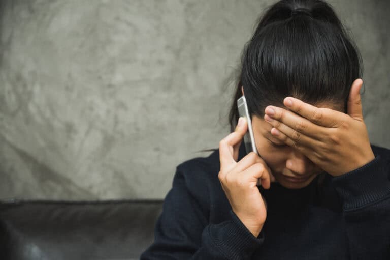 A stressed person sits on a couch, covering their forehead while discussing longshore claims mediation over the phone.