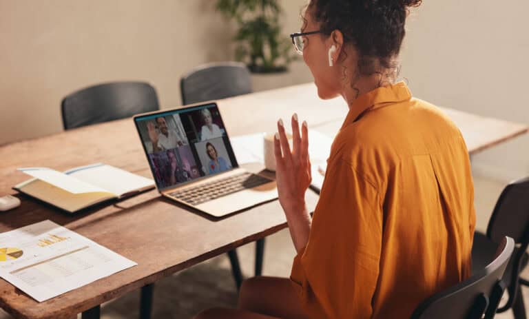 A person with glasses joins a video call about workers’ compensation mediation at a wooden table covered in papers and a notebook.