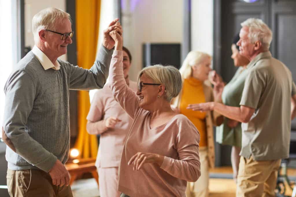 Older adults dance and socialize indoors, smiling as they take a break from workers’ compensation mediation talks.