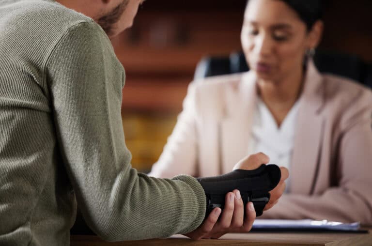 A person with a wrist brace explains their workers’ compensation case to an attentive listener at a mediation table.