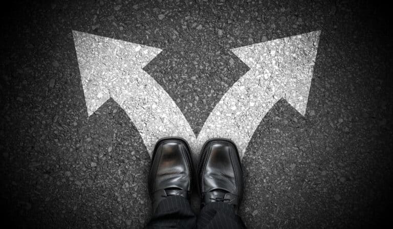 A person in black dress shoes stands at a fork, deciding on workers’ compensation mediation as two arrows point apart.