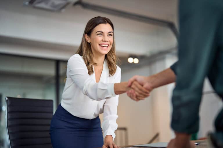 Smiling woman in business attire shakes hands in an office, reflecting a successful legal mediation outcome.