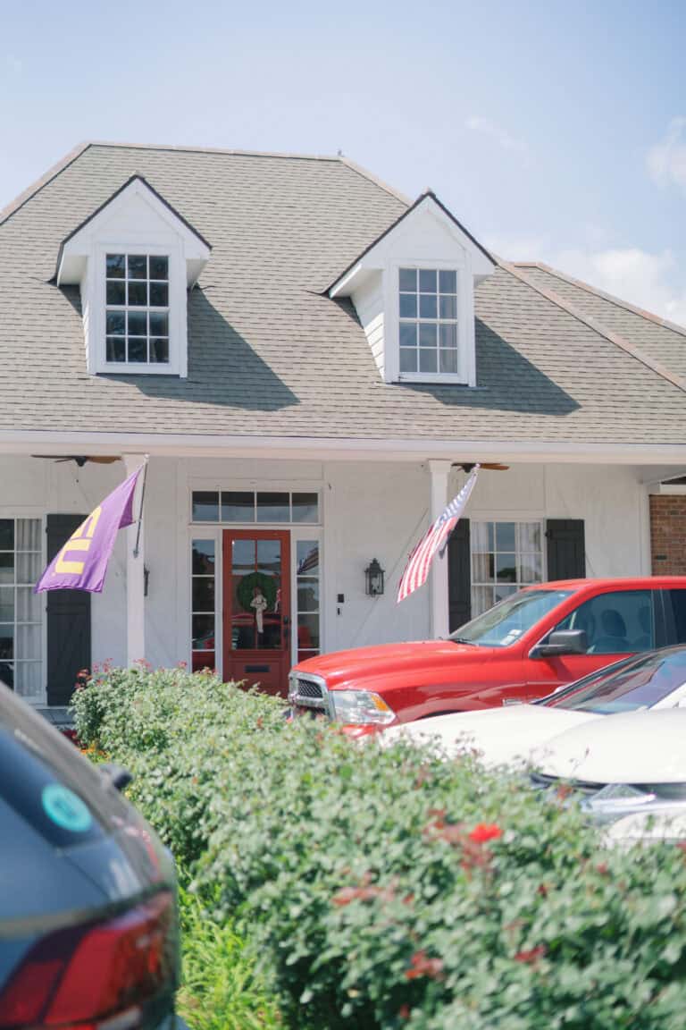 A white house with dormer windows and flags offers workers’ compensation mediation; cars and bushes are in front.
