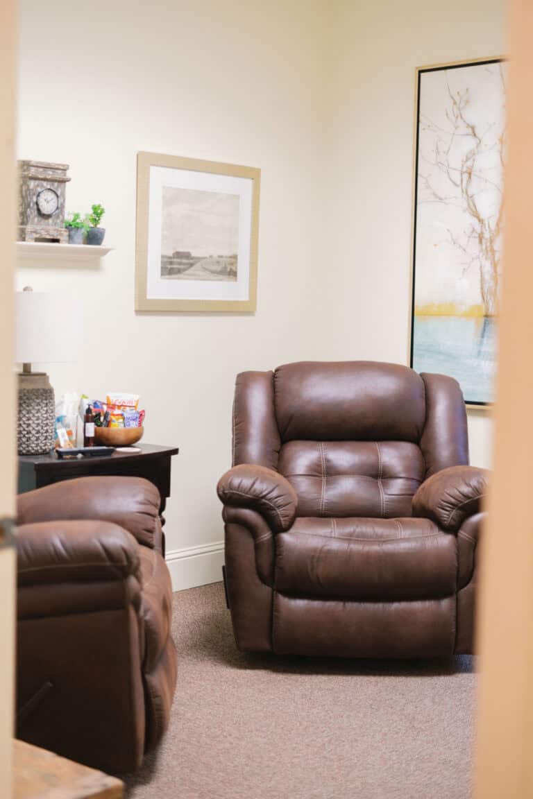 Two brown leather recliners in a cozy room with framed art, a small table, and snacks arranged for a welcoming atmosphere.