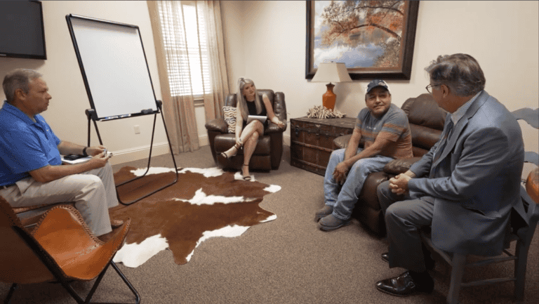Four adults talk about mediation services in a stylish office with a whiteboard, animal hide rug, and wall art.