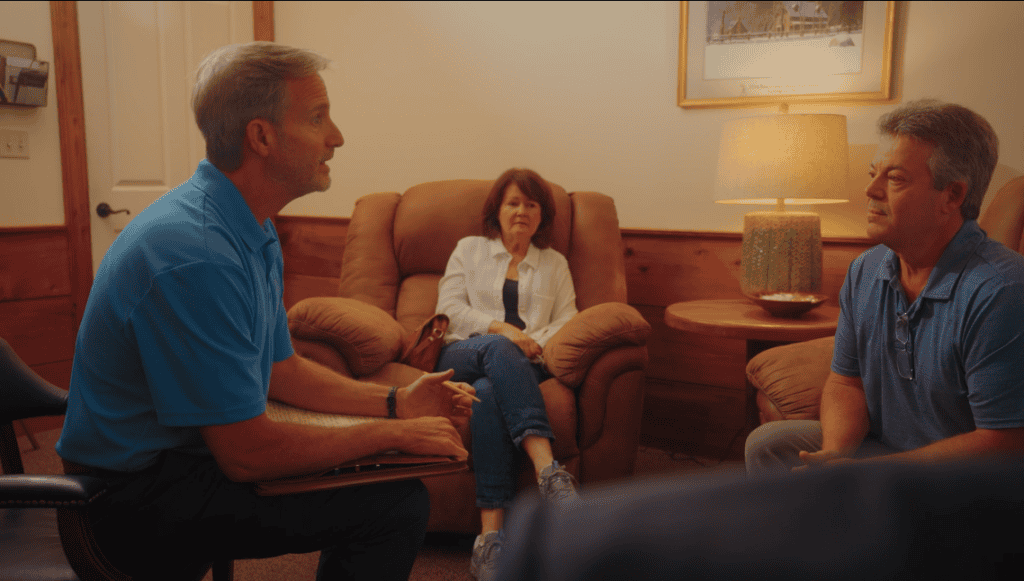 Three adults in a warmly lit room participate in a workers’ compensation mediation; two men talk while a woman observes.