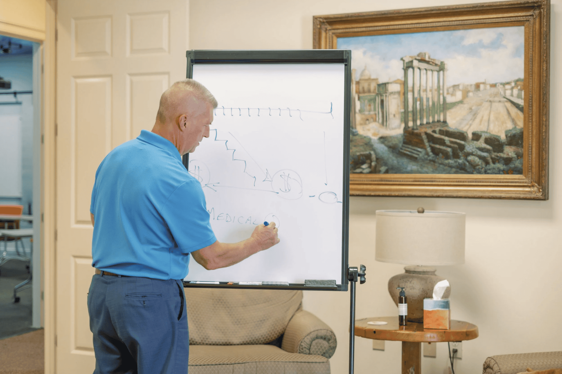 A man in a blue shirt explains workers’ compensation mediation, writing on a whiteboard in an office.