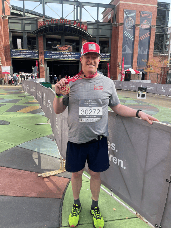 A man stands outside a stadium, proudly holding a medal and race bib, celebrating success after mediation for harbor claims.