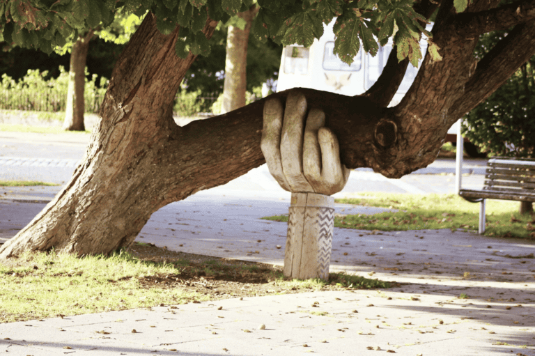 A hand sculpture holds up a tree branch by the sidewalk, evoking support much like mediation services offer in tough times.