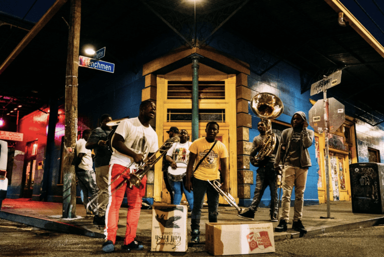 A brass band performs on a street corner near legal mediation services, with tip boxes and a brightly lit building nearby.