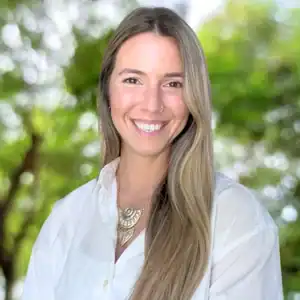 A smiling woman with long, straight hair in a white shirt stands outdoors among sunlit trees, reflecting legal mediation services.