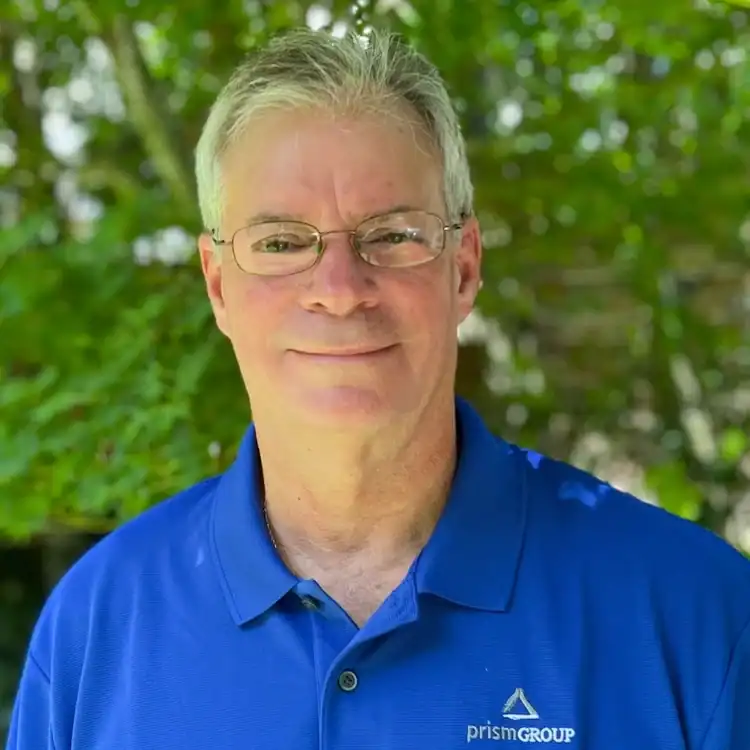 Man with short gray hair and glasses in a blue polo stands outside among green trees, known for legal mediation expertise.