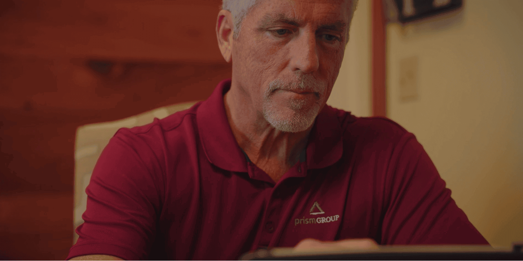 A gray-haired man with a goatee in a maroon Prism Group polo reviews legal mediation details on his tablet.