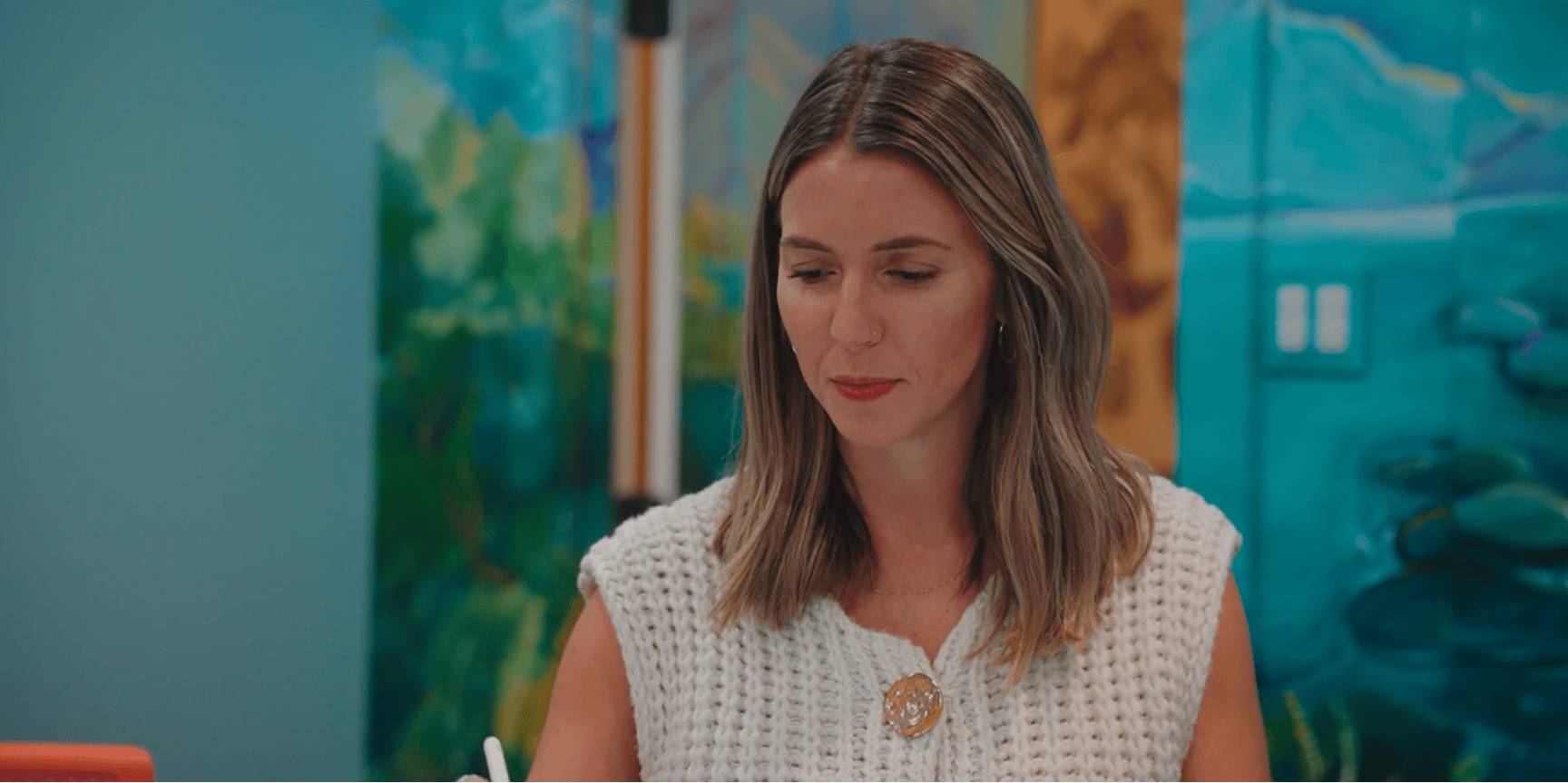 Woman with long, light brown hair sits indoors in a white top, softly lit by a mural—suited for casualty mediation discussions.