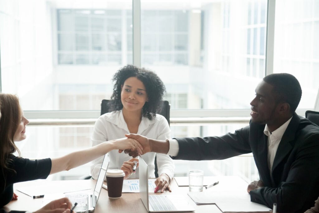 At a workers’ compensation mediation, two professionals shake hands as a third person looks on and smiles approvingly.