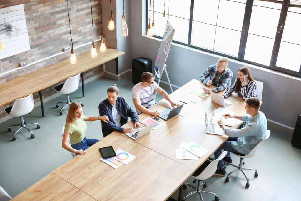 Six people work together in a modern office, reviewing charts and using laptops around a table during mediation services.