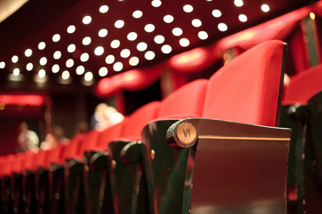 Empty red theater seats glow under round lights, with a single seat VI standing out, reminiscent of a mediation case.