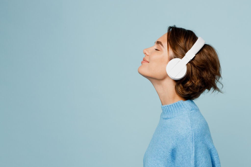 Woman in white headphones and a blue sweater relaxes, capturing the calm often found through mediation services.