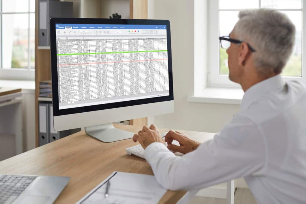 A man in an office studies a spreadsheet on his desktop, analyzing data for workers’ compensation mediation cases.