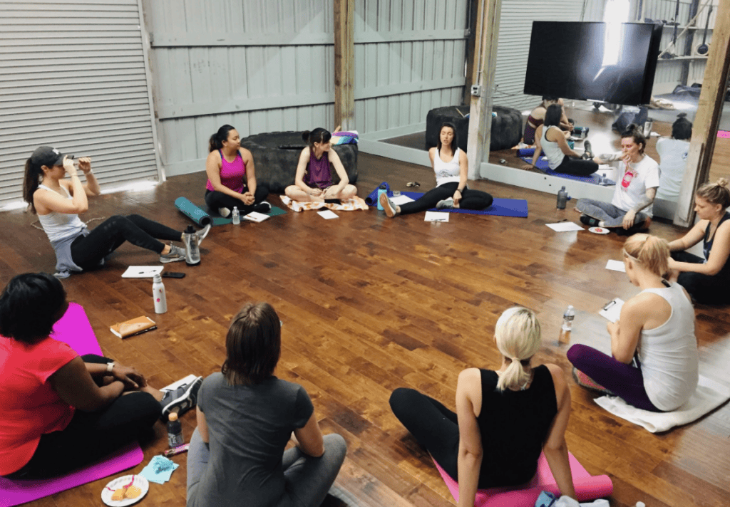 Women on yoga mats in a gym chat and share snacks after a longshore and harbor claims mediation session.